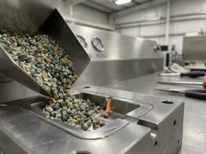Gerecyclede plastic pellets in groen en grijs tinten die in een stalen injectiegietmal stromen, gesmolten materiaal zichtbaar bij de poort.