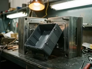 Antracietgrijs elektrische behuizing uit stalen spuitgietmal op werkbank, met geribbelde wanden en snap-fit details.